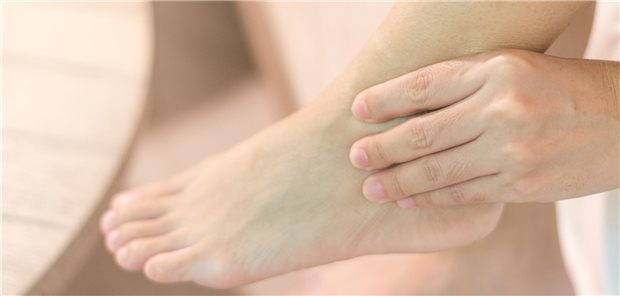 Eine Person hält mit sich mit ihrer Hand den Fußknöchel aufgrund von Schmerzen an der Achillessehne.